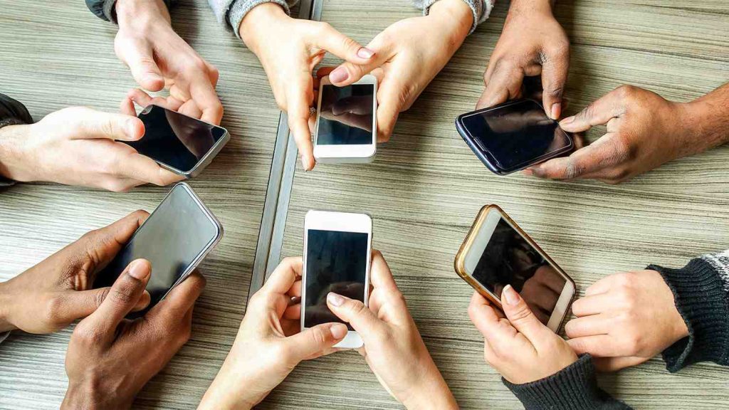 The hands of 6 employees using their business mobile phone models in a group