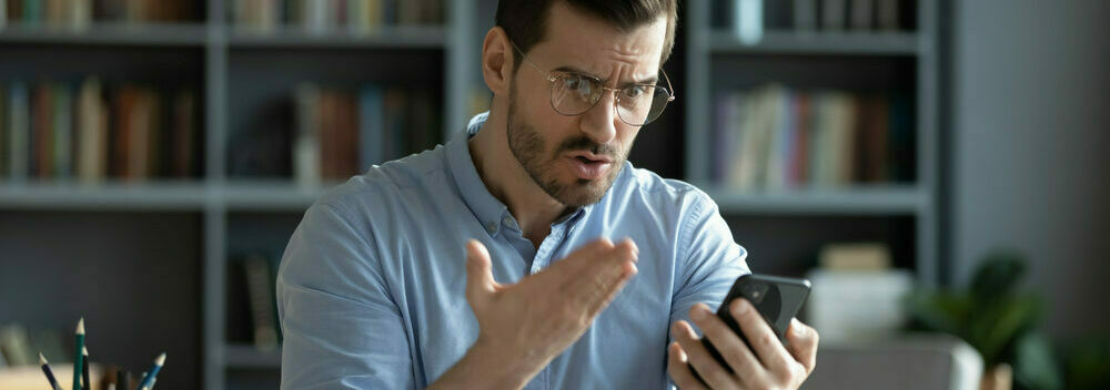 Frustrated man sits at desk and wonders why his phone is so slow