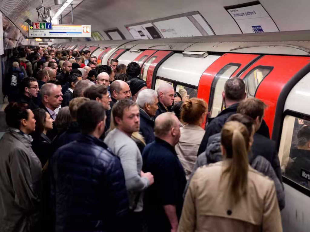 Large group of commuters board train stopped at a busy station 