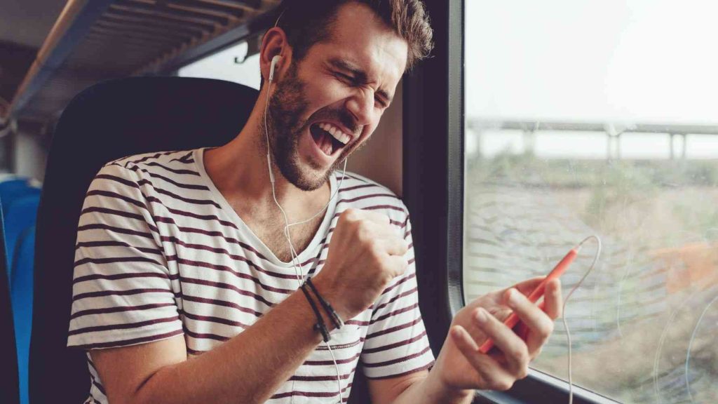Very happy man cheers whilst using his mobile smartphone on a moving train