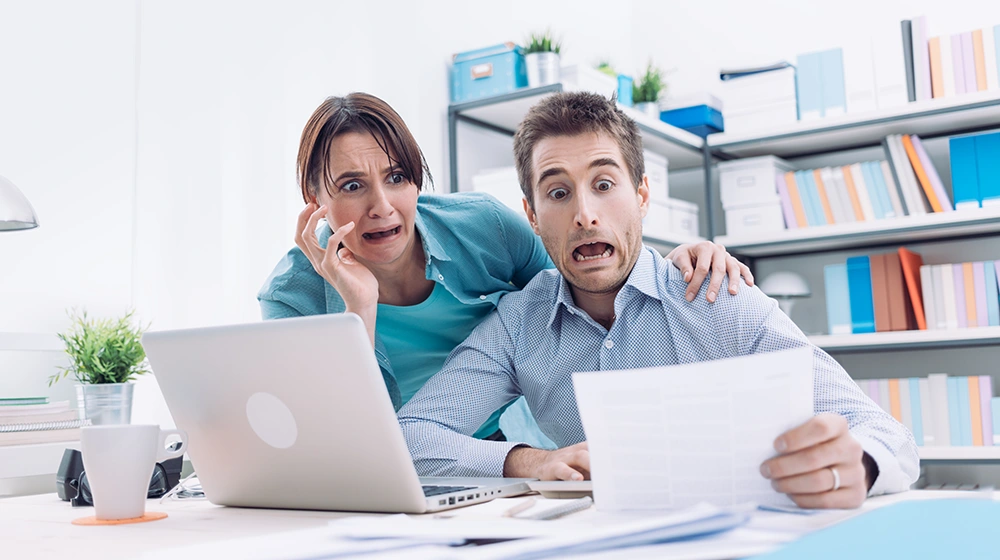 Dramatic shot of married couple in home office reading their latest bill with a mortified expression