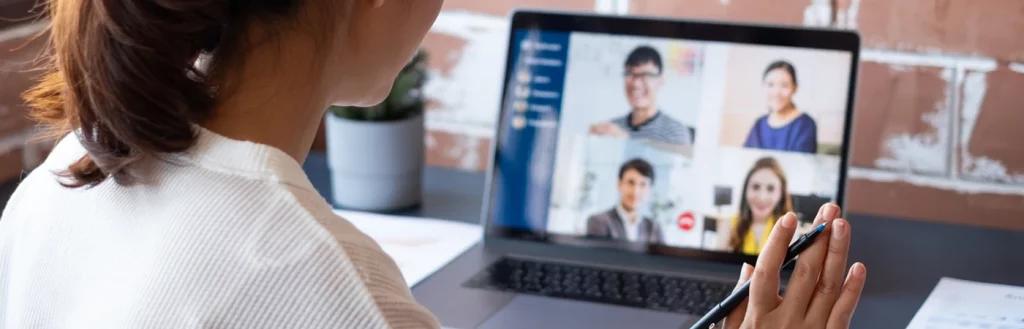 Woman holding pen waves at business colleagues during video conference call