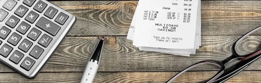 Glasses, pen, calculator, and bill receipt sit on top of wooden desk