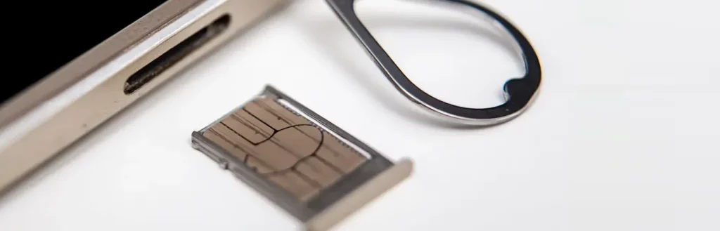 Close-up shot of open SIM card tray with SIM card inside, next to ejection pin and smartphone