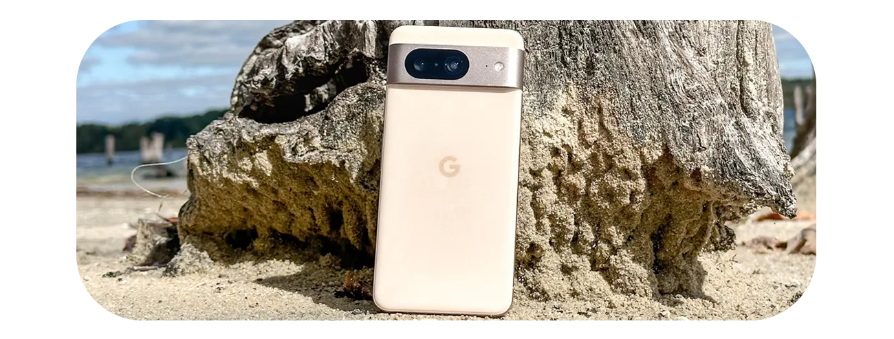 Pink Google Pixel 8 standing against a rock at the beach showing dual camera system