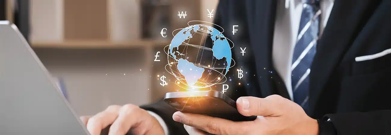 Business professional using a smartphone and laptop with global currency symbols, illustrating international business communication and mobile expenses
